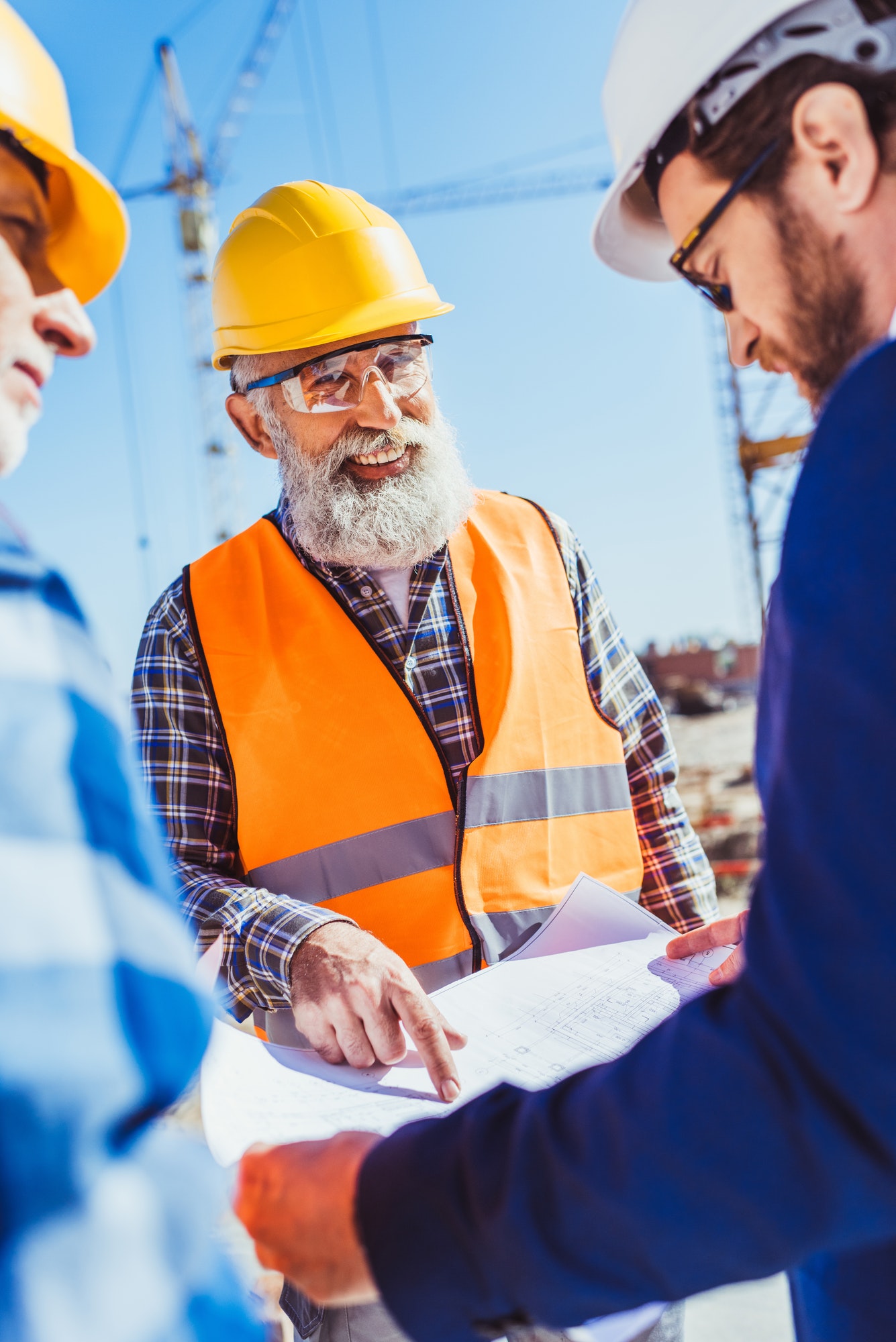 Construction worker in protective uniform discussing building plans with businessman in hardhat and